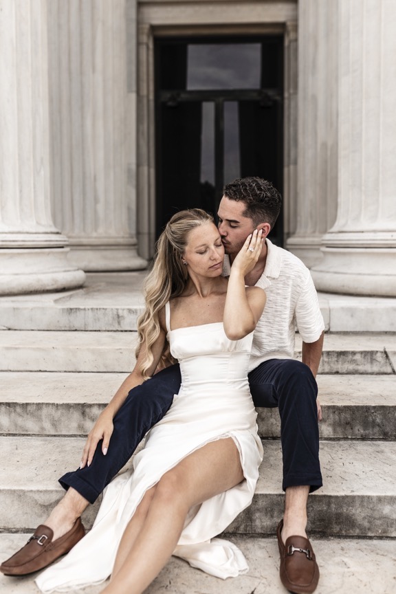 Bride and groom sitting together on stone steps, groom kissing bride's cheek